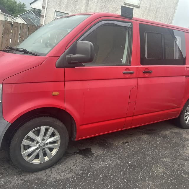 Red Volkswagen van viewed from the side on a driveway.