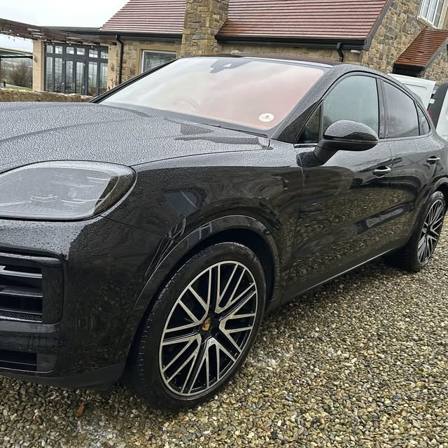 Black Porsche SUV photographed from the front-left side on a gravel drive.